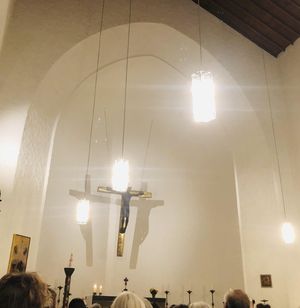 Blick in der Kirche schräg oben Richtung Altar. Zu sehen, Kreuz, Lampen, ein Teil der Decke.