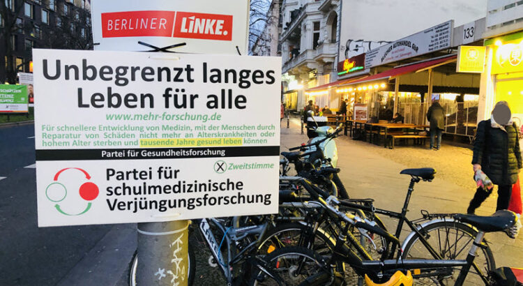 Plakate der Partei für schulmedizinische Gesundheitsforschung mit dem Slogan "Unbegrenzt langes Leben für alle".- Im Hintergrund Berliner Straßenszene.