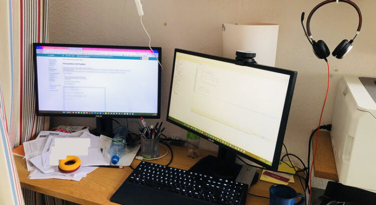 Blick auf den unaufgeräumten Schreibtisch mit Tastatur und zwei Monitoren.