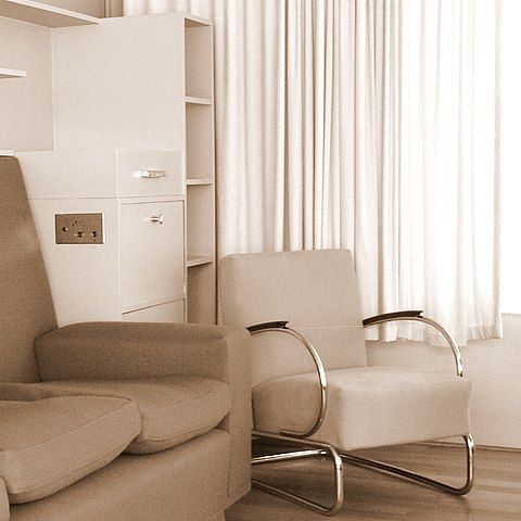 Inneneinrichtung von Huis Sonneveld. Beiger Designerstuhl neben beiger Couch auf beidem Teppich vor beiger Wand.