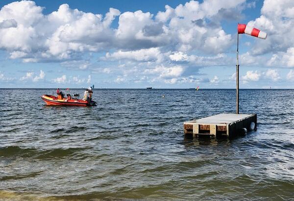 Ostsee mit Schlauchboot der Seenotrettung und Plattform mit WIndsack. Im Hintergrund ein Containerschiff.