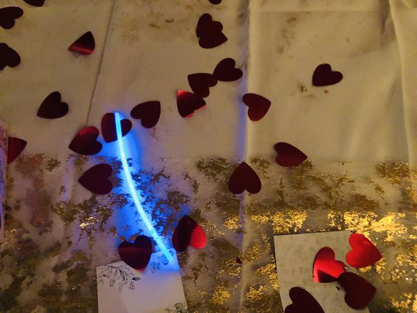 Hochzeitstafel mit Tischdecke, goldenerm Überzeug, roten glitzendernden Papierherzen und einem Leuchtelement.
