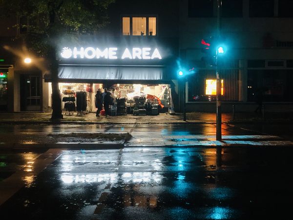Ladenschild "Home Area" und grüne Ampfeln bei strömendem Regen in Nachtdunkelheit.
