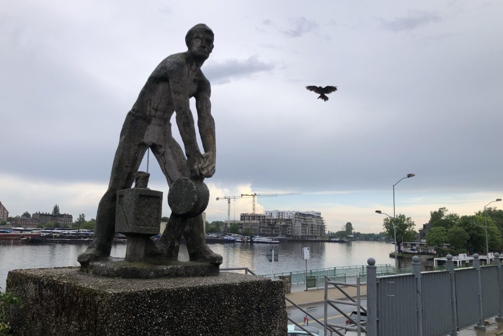 Statue eines Bahnarbeiters, im Hintergrund die Oder und ein fliegender Vogel mit gespreizten Federn.