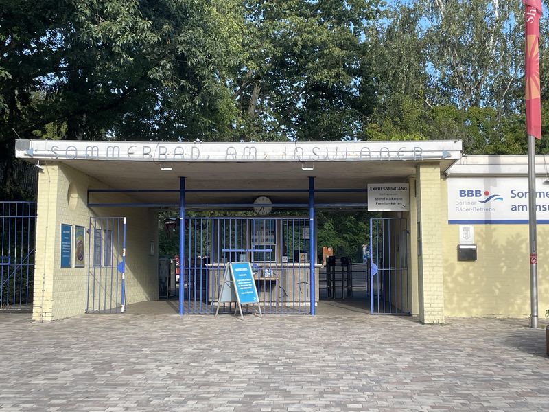 Eingang zum Sommerbad am Insulaner. Ein schmales Kassenhäuschen, unter einem Dach mit zwei Durchgängen links und rechts.