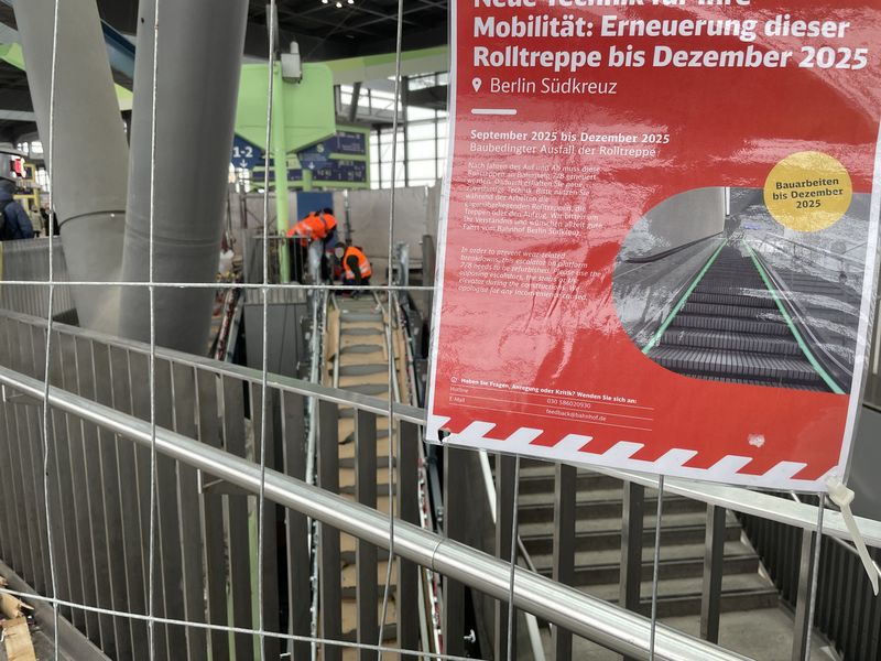 Bild einer Rolltreppen-Baustelle. Die Baustelle abgesperrt, die Rolltreppe nur noch in Teilen vorhanden, drei Gestalten in der Ferne mit Warnweste. Dazu ein Schild "Erneuerung der Rolltreppe bis Dezember 2025." Aufgenommen wurde das Bild im Februar 2026. 