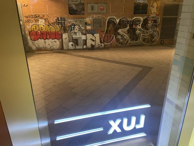 Blick aus dem Delphi Lux Kino. Vor dem Fenster eine abendlich beleuchtete Wand mit Graffitti und ein schmaler Weg. Im Fenster spiegelt sich der Schriftzug "Lux"