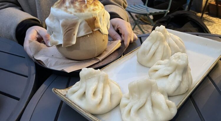 Ein Teller mit Khinkali und ein Gefäss mit überbackenen Teigtaschen auf einem Tisch,