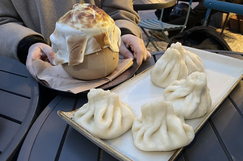 Ein Teller mit Khinkali und ein Gefäss mit überbackenen Teigtaschen auf einem Tisch,