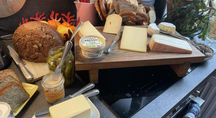 Verschiedene Käse, Brot, veganer Schmalz und Gebäck auf Buffet.