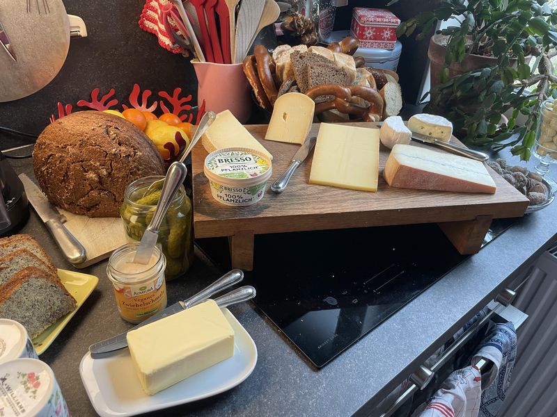 Verschiedene Käse, Brot, veganer Schmalz und Gebäck auf Buffet.