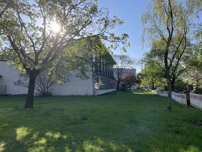 Stadtbad von 1961 auf sattgrüner Wiese mit Bäumen vor Frühlingssonne.