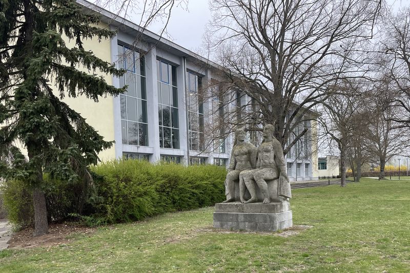 Sportforum Hohenschönhausen. Schräg seitlicher Blick auf die Schwimmhalle und die Plastik davor. 