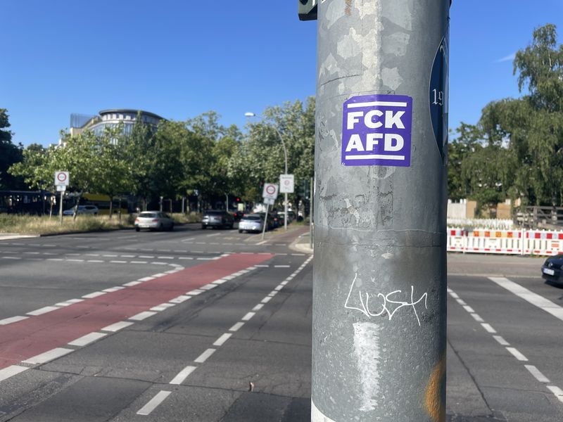 Ampelpfahl mit lila Aufkleber "FCK AFD". Dahinter eine Kreuzung, 